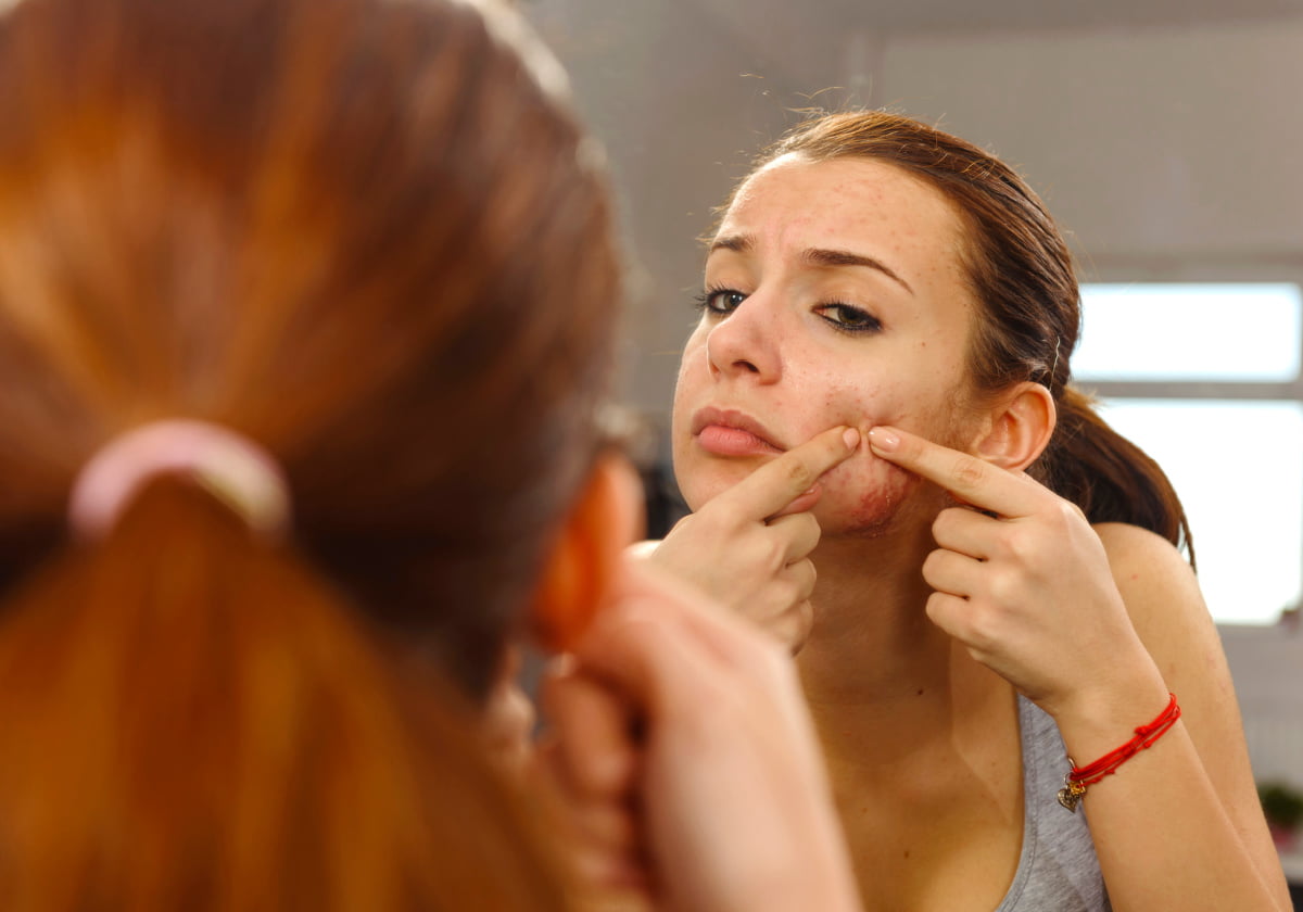 Teenage girl concerned about skin issues in the mirror before dermatologist