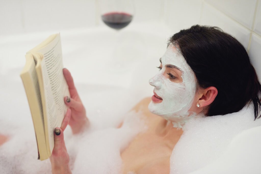 Woman with Face Mask doing Skincare While Reading and Drinking Wine in Bath